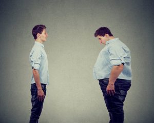 Young slim fit man looking at himself with morbid obesity
